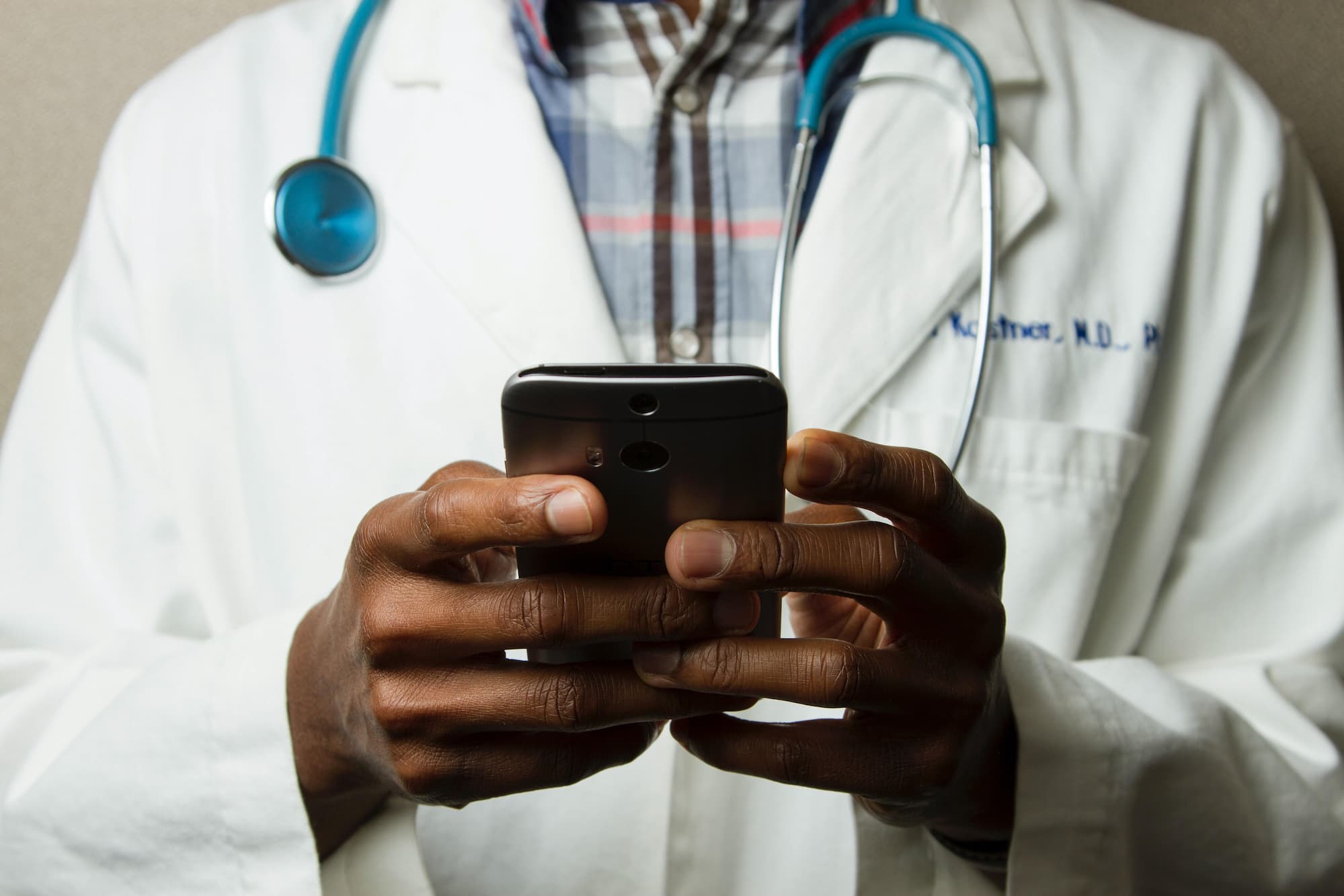 A doctor holding a smartphone with a medical app Hands of a doctor in a while overall, with a stethoscope around his neck, holding a smartphone